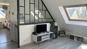 A modern loft bedroom with a TV, bookshelf, and a skylight. - Maison Récente T5 Herbignac Proche Guerande (Herbignac)