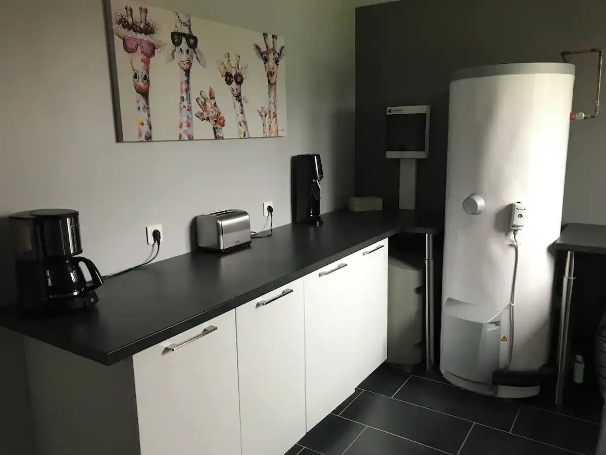 Une cuisine moderne avec un plan de travail noir, des meubles blancs, une machine à café, un grille-pain et un chauffe-eau.