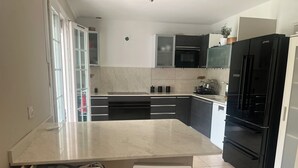 A modern kitchen with a central island, black appliances, and white cabinetry. - Spacious and modern 4 bedroom 2 bathroom House with garden ideal fir families  (Villejuif)
