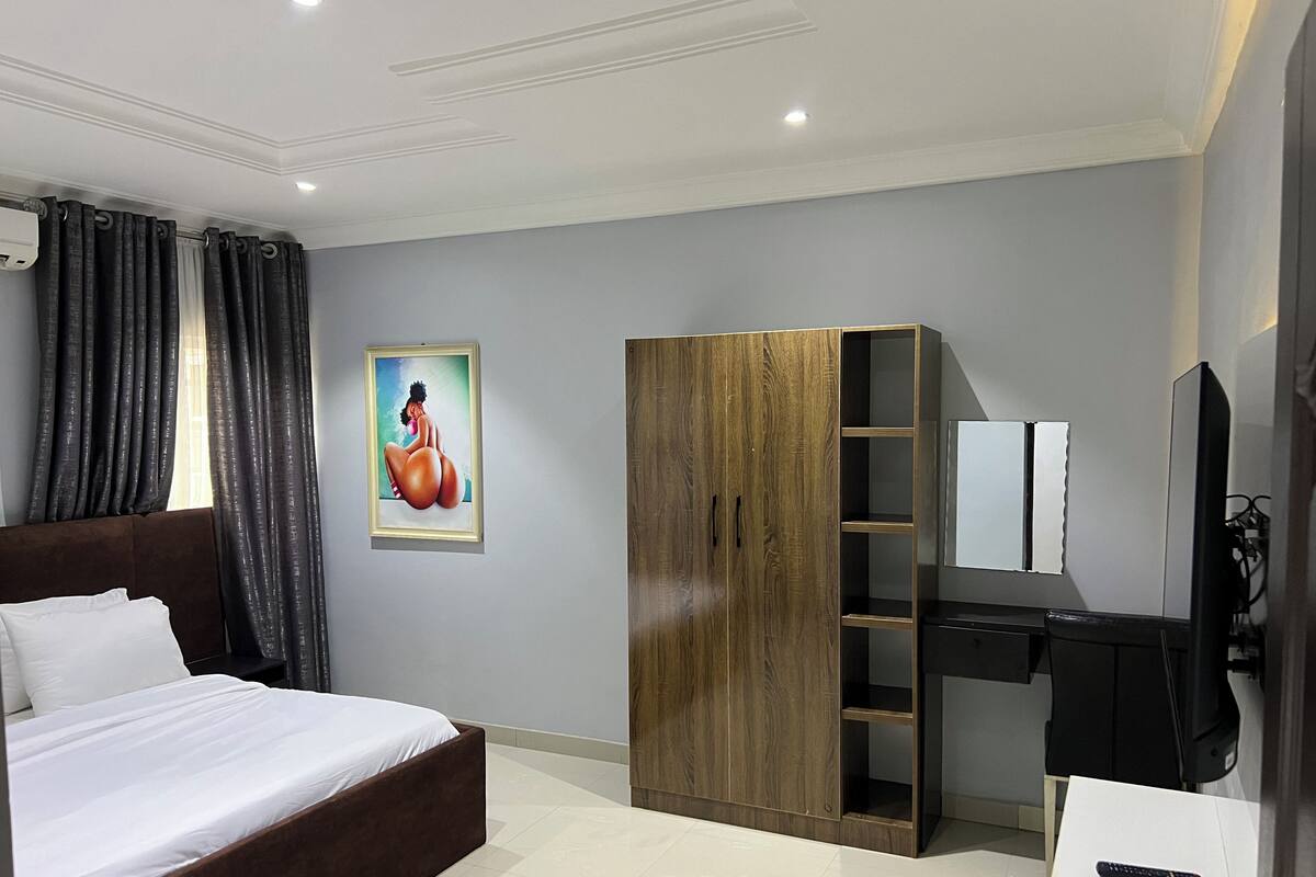 A bedroom with a bed, a wardrobe, a desk, and a TV.