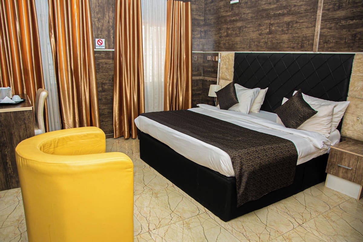 A hotel room with a large bed, a yellow armchair, and a wooden headboard.