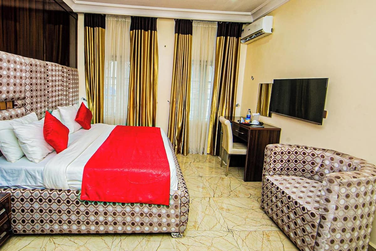 A hotel room with a patterned bed, a desk with a chair, a television, and curtains.