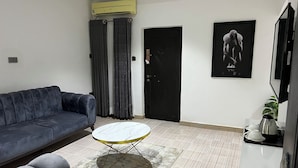 A living room with a sofa, a round coffee table, a black door, and a framed picture on the wall. - Apartment 550 (Abuja)