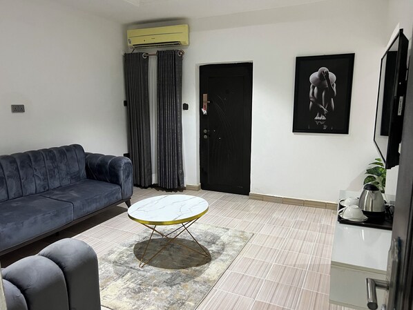 A living room with a sofa, a round coffee table, a black door, and a framed picture on the wall.