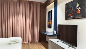 A modern hotel room with a large bed, a flat-screen TV, a console table, and a painting on the wall. - Tatvam Villa (Sohna)