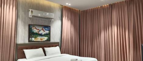 A modern hotel room with a large bed, a ceiling fan, an air conditioning unit, and a painting on the wall.
