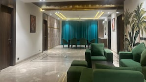 A spacious lobby with a marble floor, green seating area, teal curtains, and a ceiling with recessed lighting. - Tatvam Villa (Sohna)