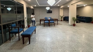 A modern lobby with a central seating area, a chandelier, and a person standing near the entrance. - Tatvam Villa (Sohna)
