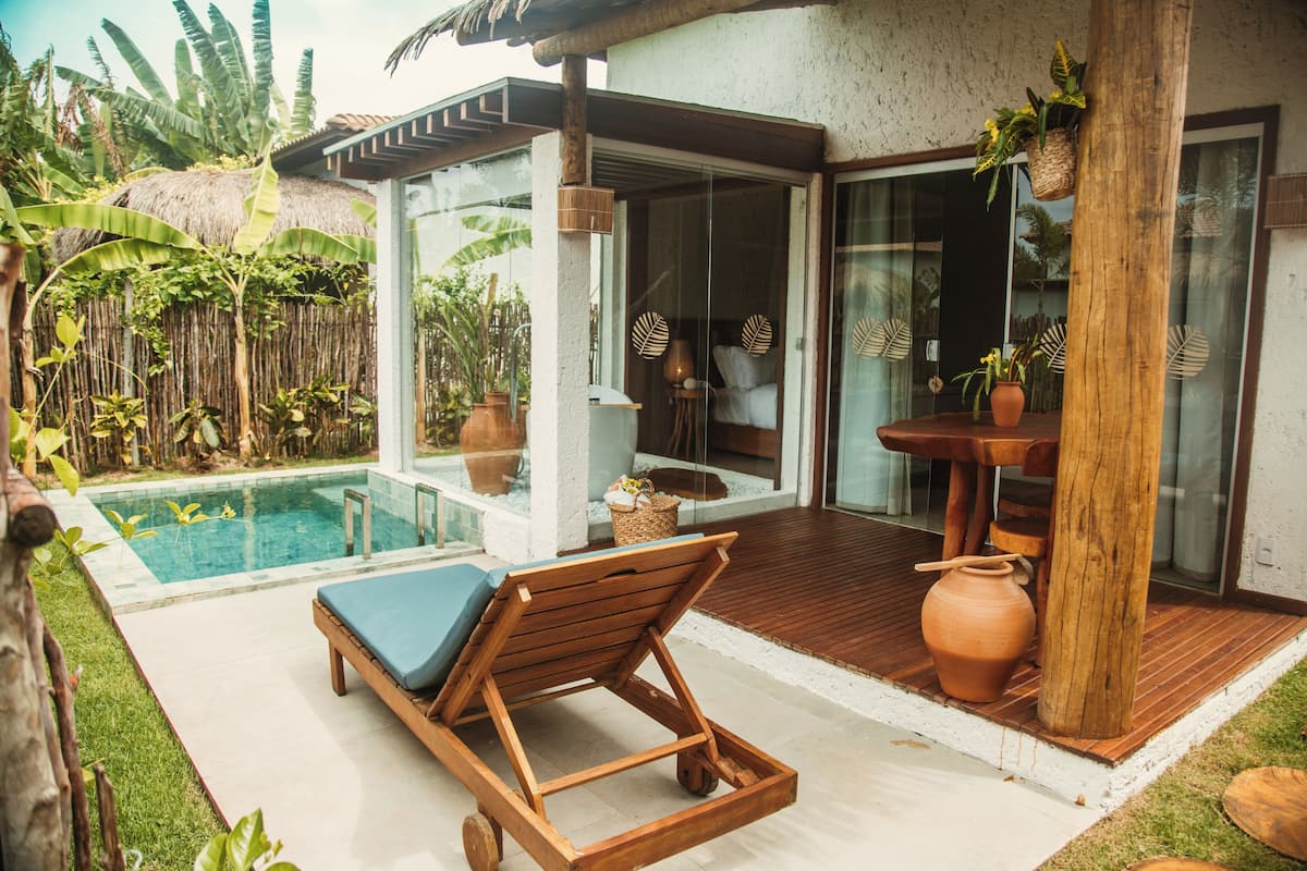 A poolside area with a lounge chair, a wooden deck, and a glass door leading to a room.