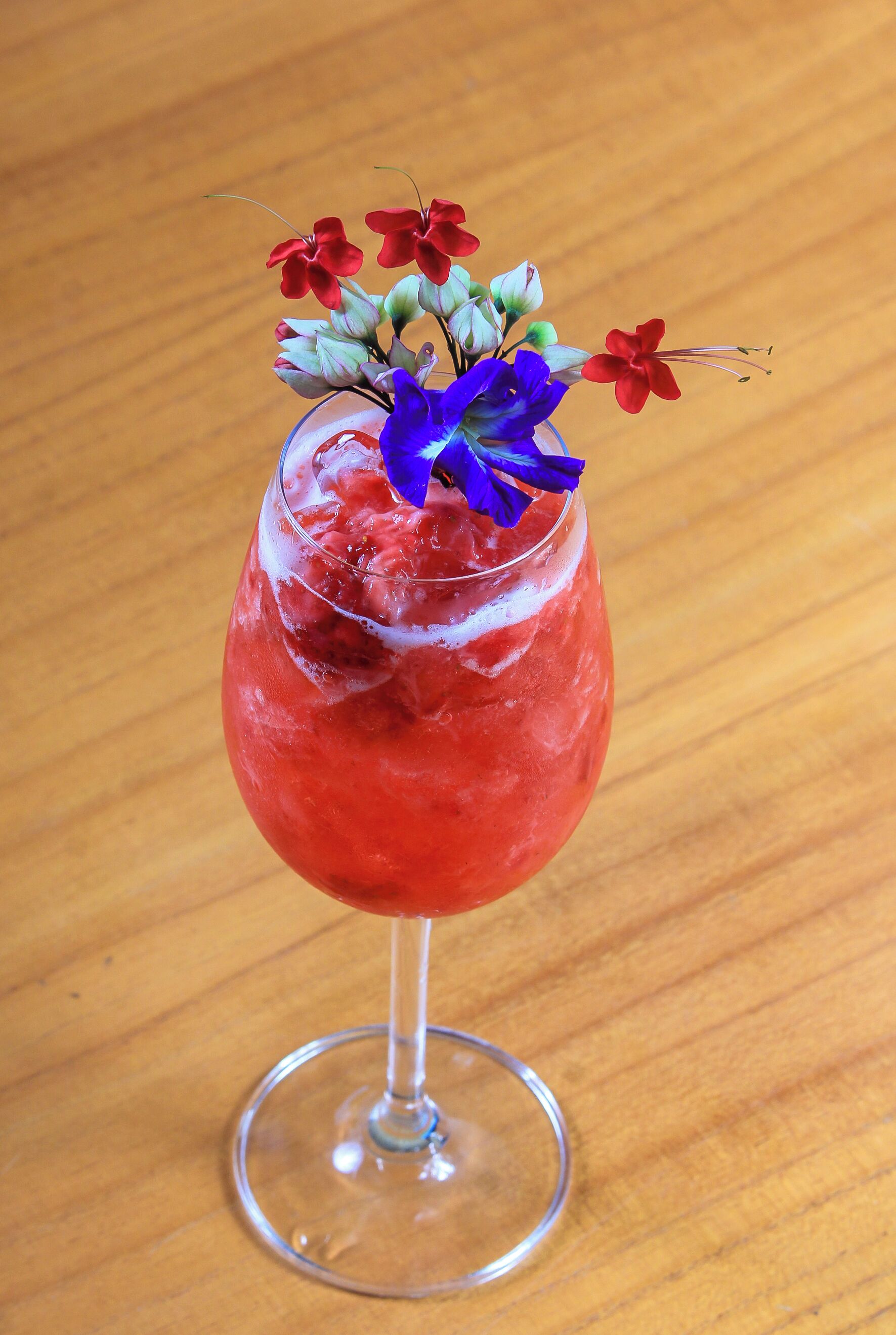 A cocktail in a stemmed glass with a red liquid and decorative flowers.