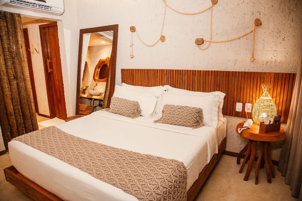 A hotel room with a large bed, wooden headboard, a bedside table with a lamp, and a mirror on the wall.