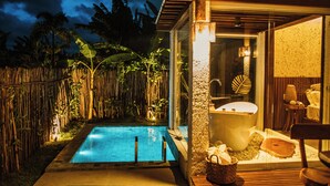 Une piscine entourée d’une clôture en bambou, un espace de spa clos par des parois de verre avec une baignoire, et une terrasse en bois.