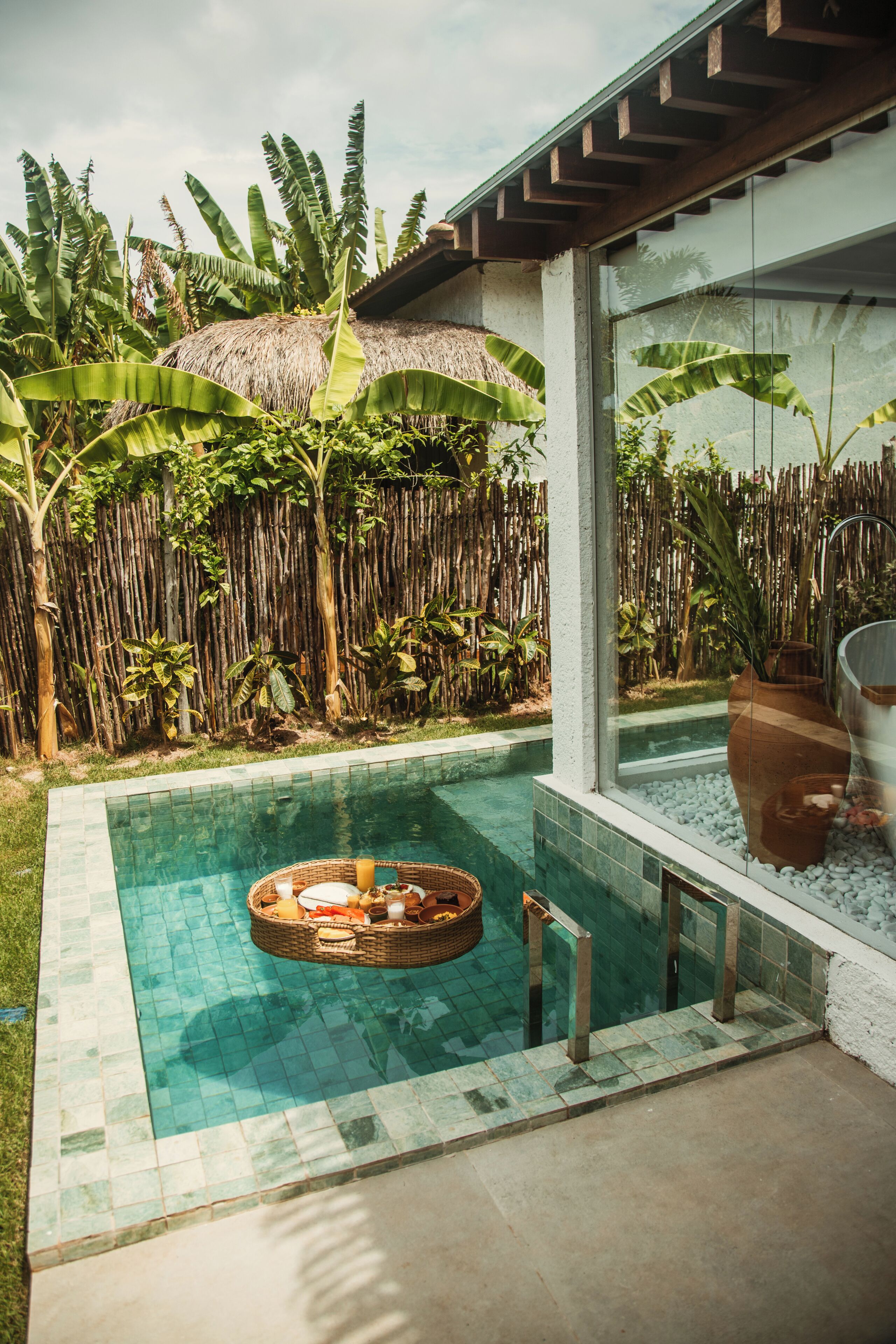 A pool with a hot tub, surrounded by lush vegetation and a bamboo fence.