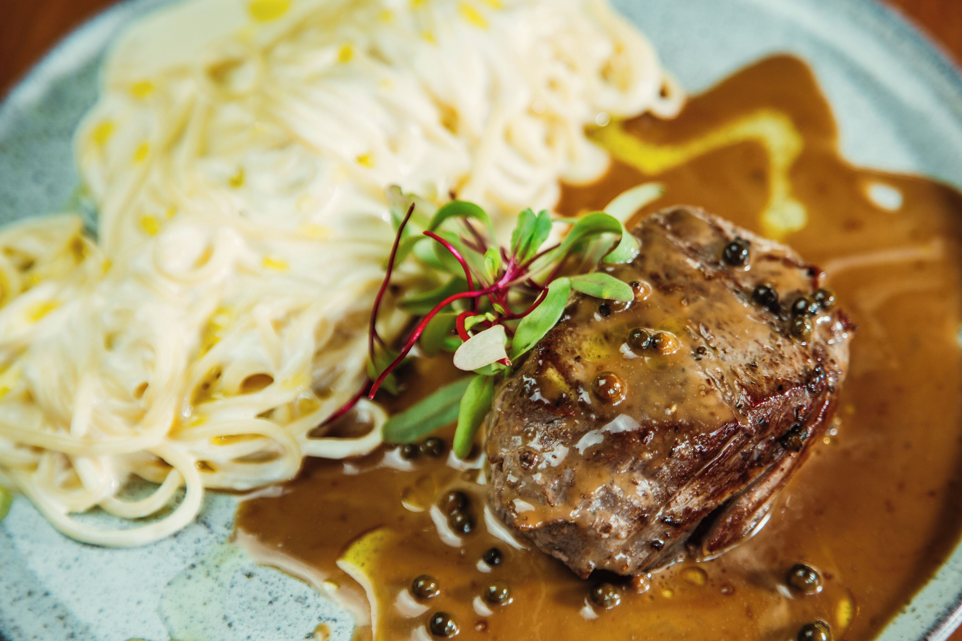 A plate with a steak, sauce, and noodles.