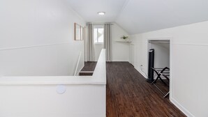 Un interno moderno e minimalista con pavimento in legno, pareti bianche e una scala che conduce a un piano superiore.