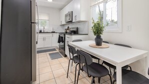Una cucina moderna con mobili bianchi, un frigorifero nero, un forno a microonde e un'area pranzo con tavolo bianco e sedie nere.