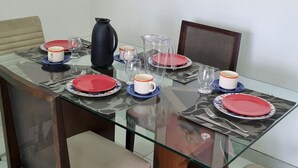 A dining table set with plates, glasses, and a pitcher, surrounded by chairs with cushioned seats. - Apto Próximo ao Pátio do Forró (Maurício de Nassau Caruaru)