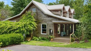Une maison rustique en bois, dotée d’un toit à forte pente, d’un porche avec des sièges d’extérieur et d’un jardin bien entretenu.
