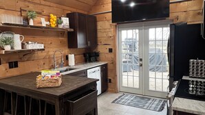 Une cuisine avec des murs en bois, un îlot central, un téléviseur à écran plat et une porte-fenêtre coulissante donnant sur l’extérieur.