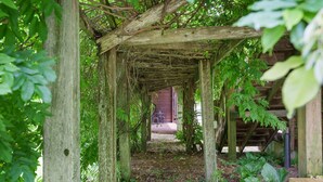 Une structure de pergola en bois avec un chemin menant à l’entrée d’un bâtiment.