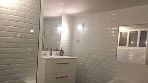 A bathroom with white subway tiles, a white vanity with drawers, a mirror, and a bathtub.