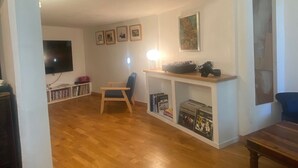 A spacious living area with a wooden floor, a television mounted on the wall, a bookshelf, and a blue sofa.