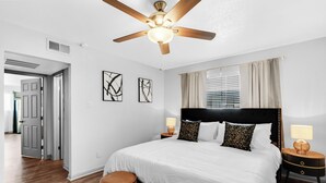 Un dormitorio moderno con una cama grande, un ventilador de techo y una mesita de noche con lámpara.