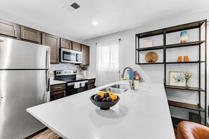 A modern kitchen with stainless steel appliances, a white countertop, and a bowl of fruit.
