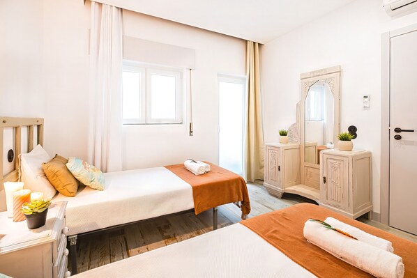 A room with two beds, a mirror, a cabinet, and a window.