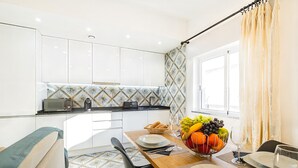 A modern kitchen with white cabinets, a tiled backsplash, and a dining area with a table set for two. - Apartment with sea view in Carvoeiro (Carvoeiro)