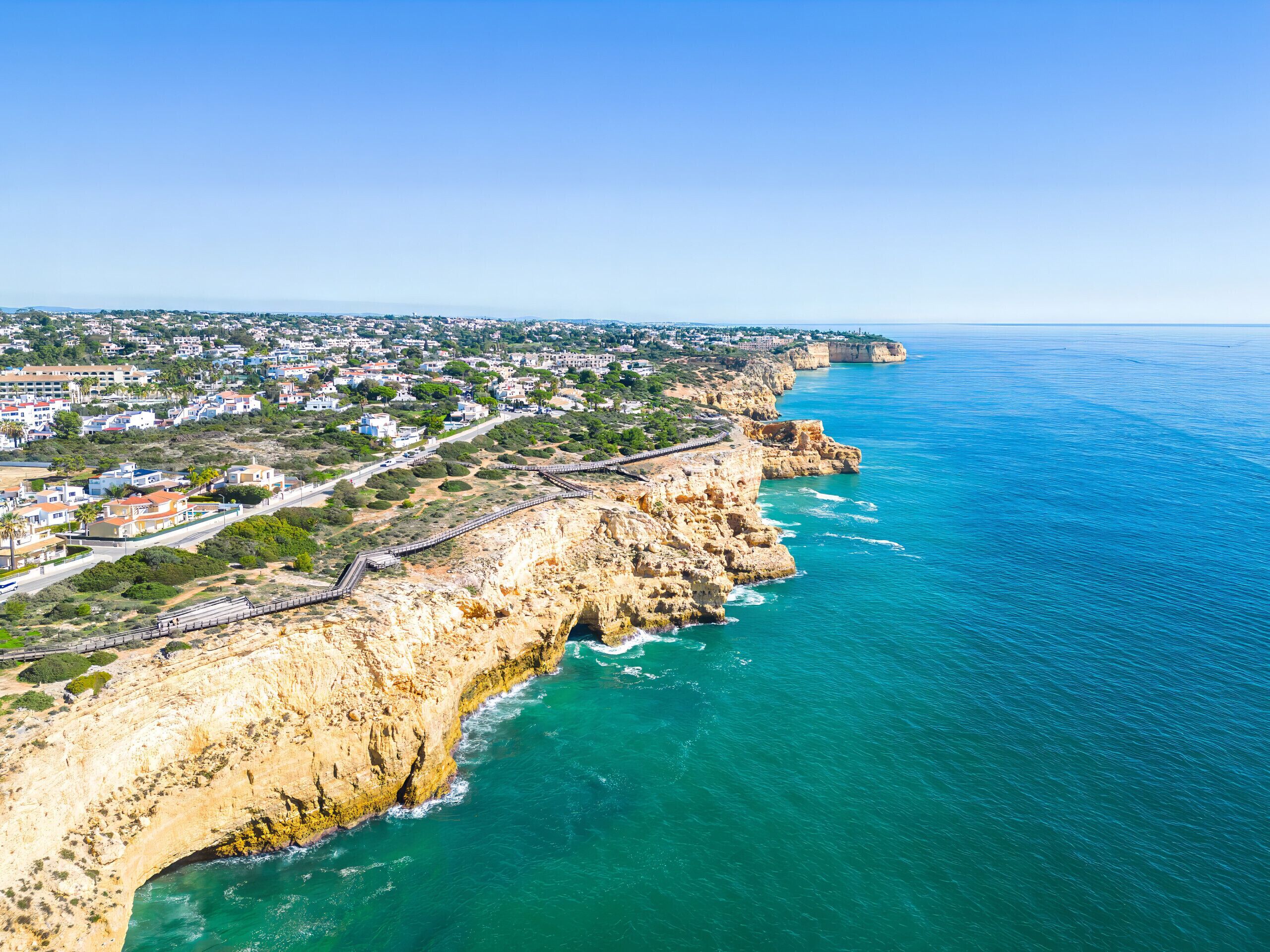 A coastal town with a prominent cliff, a paved walkway along the edge, and a view of the sea.