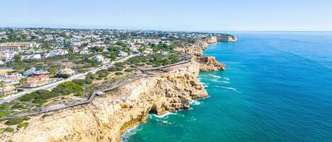 A coastal town with a prominent cliff, a paved walkway along the edge, and a view of the sea.
