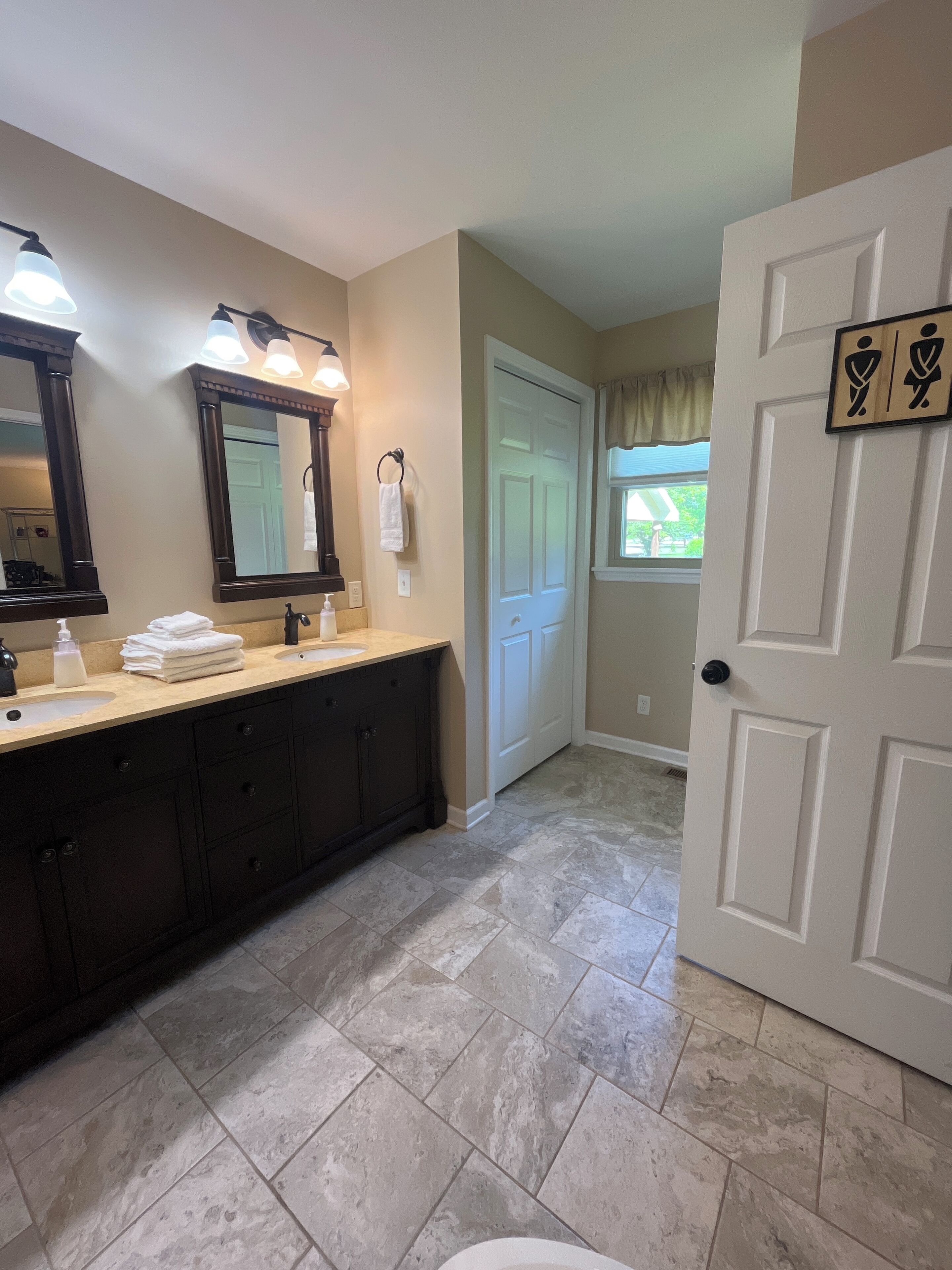 A bathroom with a double sink vanity, a large mirror, and a door with a towel rack.