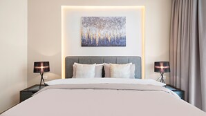 Een hotelkamer met een groot bed, twee nachtkastjes met lampen, een hoofdeinde en een kunstwerk aan de muur.