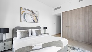 A modern bedroom with a large bed, bedside lamps, a grey headboard, a wooden wardrobe, and a large abstract painting on the wall. - Oxford 212 - 303 2BD (Dubai)