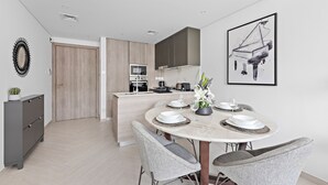 A modern kitchen with a central island, a dining area with a round table and wicker chairs, and a framed artwork on the wall. - Oxford 212 - 303 2BD (Dubai)