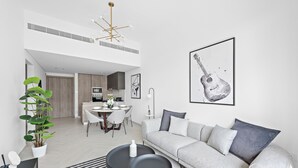 A modern living room with a grey sofa, a dining area, and a kitchen in the background. - Oxford 212 - 303 2BD (Dubai)