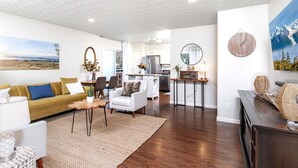 A modern living room with a sofa, armchair, and coffee table, a kitchen area, and a dining space.