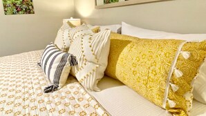 A hotel room with a bed, pillows, a wall-mounted mirror, and a framed picture.