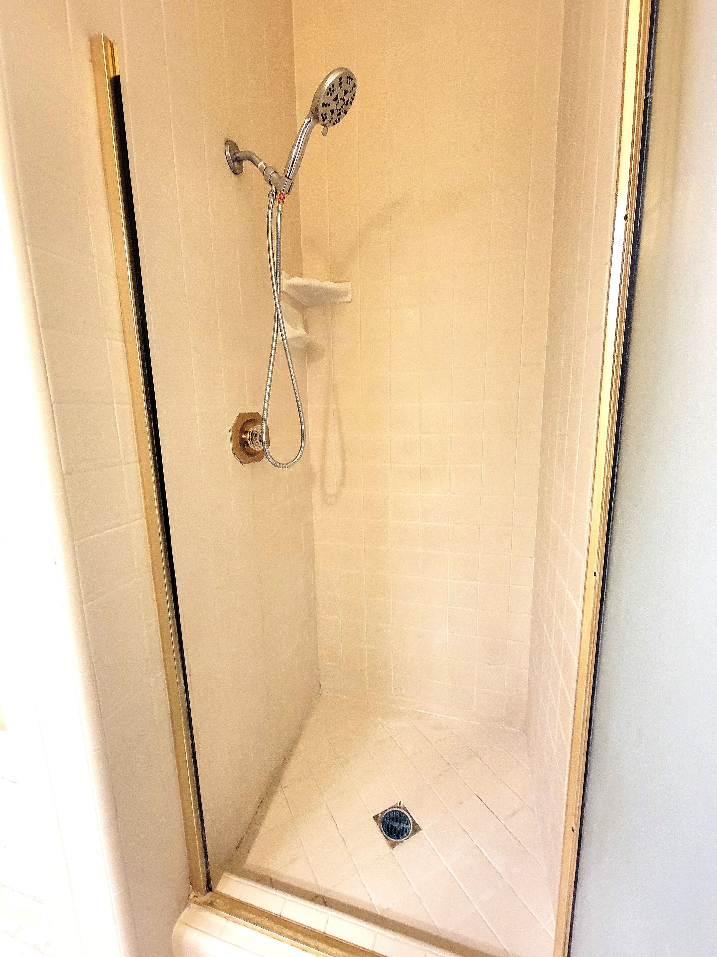 Een douche met een handdouche en een bediening aan de muur.