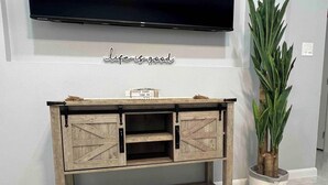 Un mueble de madera con un televisor montado encima, un cartel motivacional y una planta en maceta a su lado.