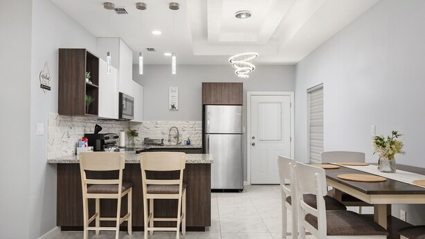 Una cocina moderna con armarios de madera oscura, un refrigerador de acero inoxidable y una salpicadera de mármol. Hay dos sillas de madera en la isla y una mesa de comedor con individuales.