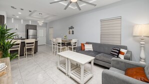 Una sala de estar moderna con un sofá gris, una mesa de centro blanca y una zona de comedor con una araña.