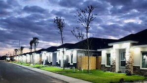 Una hilera de casas modernas de un piso, con césped cuidado e iluminación de calle.