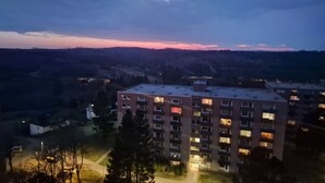 Un immeuble à plusieurs étages, avec des fenêtres illuminées, entouré d’arbres et situé dans un paysage vallonné.