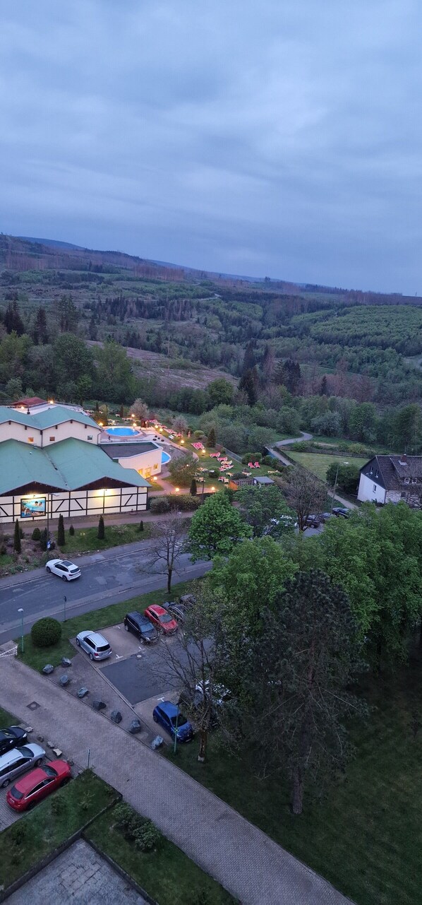 A hotel with a swimming pool, parking area, and a view of the surrounding hills.