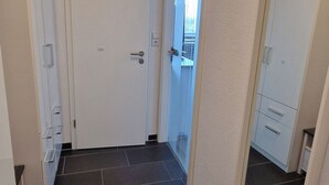 Un couloir avec un sol carrelé foncé, des murs blancs et une porte donnant sur un balcon.