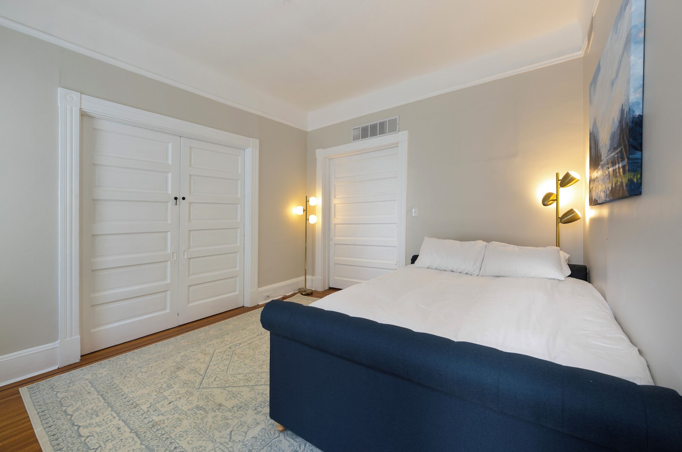 Een slaapkamer met een groot bed, twee kledingkasten, een vloerlamp en een schilderij aan de muur.