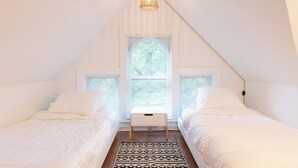 Une chambre avec deux lits, une banquette centrale et une grande fenêtre avec des stores.