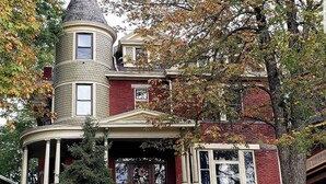 Une maison de style victorien, dotée d’une tourelle imposante, d’une véranda qui fait le tour de la maison et d’une porte d’entrée ornée d’un panneau de verre décoratif.